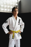 Young boy in a professional white Kids BJJ Gi with reinforced stitching and Bjjlifestyle patches in a gym training setting.