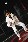 Boy in Kids White BJJ Gi Training Armor with patches and yellow belt in a wrestling stance on gym mats.