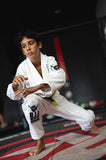 Young boy wearing a white kids BJJ gi training armor with black patches in a martial arts gym.