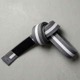 Knotted gray-white pearl weave Kids BJJ belt with rank bar and size label on gray concrete.